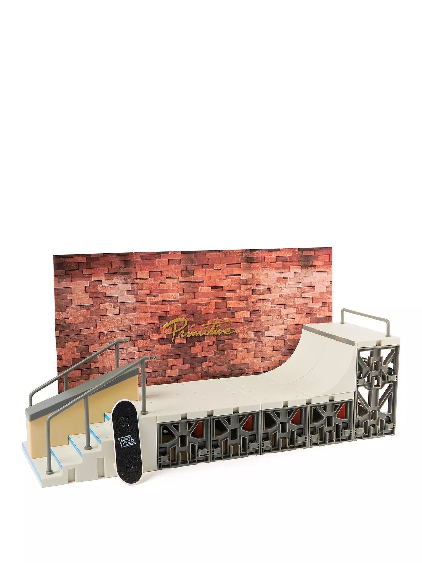 Model skateboard ramp with 'Primitive' branding against a brick wall background