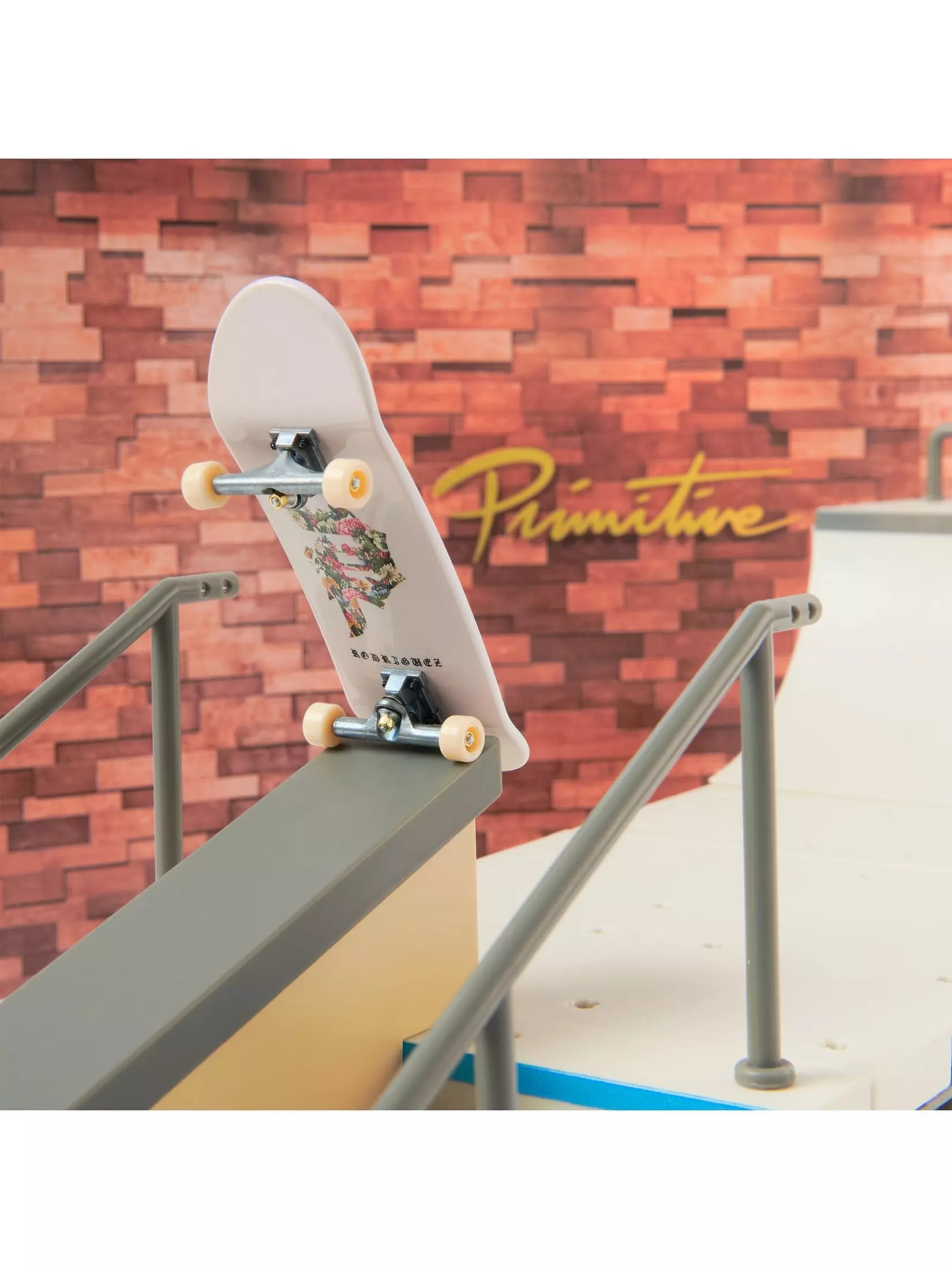 Skateboard with 'Primitive' branding on a ramp against a brick wall.